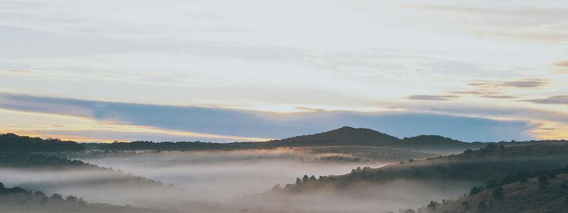 Wide panoramic shot of a person watching a sunrise over mountains.